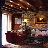 Wohnzimmer im alten Rustiko mit roter Couch und mit Kissen dekoriertes Sofa vor Natursteinwand