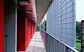 Rot getönte Hausfassade mit Laubengang und Sichtschutz aus Metallgitter