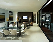 weiße Schalenstühle vor modernem Esstisch im offenen Wohnraum und offenstehender Terrassentür mit Blick auf Pool in Nachtstimmung