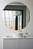 A white designer wash stand with a cupboard underneath and a round wall mirror