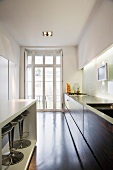 A narrow designer kitchen with a white counter in front of the cupboards