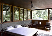 Doppelbett mit weisser Bettwäsche vor halbhoher Betonwand und Holzjalousien vor Fenster