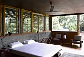 Double bed with white bed linen in front of half-height concrete wall and wooden blinds on windows