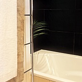 Detail of a corner of a bathroom with a bath tub and black tiles on the wall