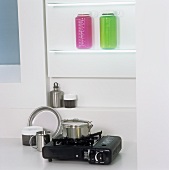 Coloured containers on a shelf above a pot on a single gas hob