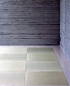 A corner of a room with exposed concrete walls and tatami mats on the floor