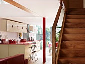 Simple wooden staircase next to open-plan kitchen with white cupboard fronts and a red painted metal pillar