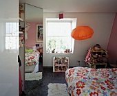 Modern child's room with pillow-shaped, orange lamp and reflection of flowered bed linen in fitted wardrobe