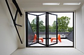 View through half-opened folding window onto roof terrace with two orange plastic chairs