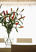 Glasvase mit rotblühendem Lilienstrauss im Gegenlicht auf modernem Esstisch