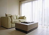 Upholstered sofa with soft cushions and cubist coffee table on a tiled floor in front of a wide window