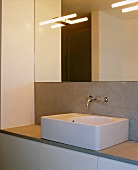 Rectangular sit-on basin with wall-mounted taps concealed in grey wall cladding under a large mirror reflecting lights