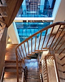 Mehrgeschossige Wohnungstreppe mit Stufen und Geländer aus edlem Holz vor Fenster im blauen Dämmerlicht