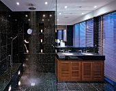 Schwarze, gesprenkelte Fliesen in modernem Bad mit Lichteffekten durch Spots, raumhohen Spiegel und Jalousie vor blauem Dämmerlicht