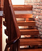 Wooden living room stairs ornamented with double grooves next to an exposed brick wall with recessed spotlights
