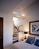 Traditional bedroom with modern painting in antique frame next to winding wooden staircase to ensuite bathroom