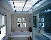 Light and shade effect through horizontal blinds covering large skylight in modern bathroom with English sash windows