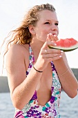 A girl eating a slice of watermelon on a beach