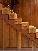 Teilweise sichtbare Person auf offener Holztreppe mit Stufen aus Vierkantholz vor Holzwand