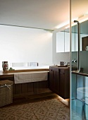 View through open glass door of wood-clad bathtub and washstand in modern bathroom