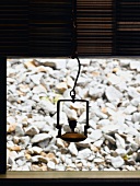 Metal vessel hanging in front of window and view of stones