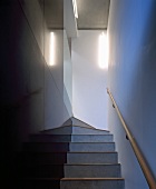 Narrow staircase with black stone-tiled wall and wooden handrail