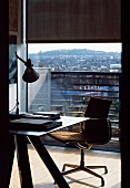 Desk with modern office swivel chair in front of ceiling-height balcony window with view of city