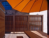 Aufgespannter gelber Sonnenschirm auf Holzterrasse und Sichtschutzzaun aus Holz