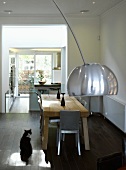 Curved lamp in front of dining area with rustic wooden table and open kitchen