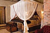 A double bed with a canopy and a trunk at the end of the bed