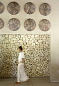 Woman walking through meditative room - wall decorations hanging on lintel above doorway and view of stone wall beyond