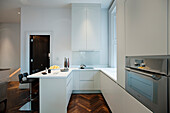 Modern fitted kitchen with white fronts and dark herringbone parquet flooring