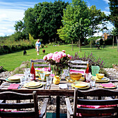 Gedeckter Tisch im Garten mit Pfingstrosen, Frau und Hunde im Hintergrund