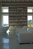 Hochregal mit Büchern und weiße Ledersessel in minimalistischem Wohnzimmer mit Betonfußboden