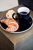 Eine Tasse Kaffee mit Croissant und Muffin auf einem schwarzen Teller
