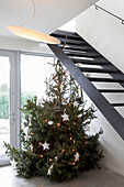 Weihnachtsbaum mit Lichterketten und weißen Sternen neben moderner Treppe
