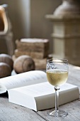 Ein Glas Weißwein neben aufgeschlagenem Buch auf rustikalem Tisch