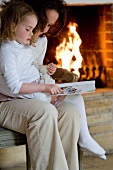 A mother and daughter reading a book in front of a fireplace