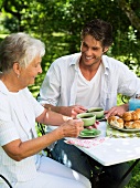 Ältere Frau und junger Mann trinken Kaffee im Garten