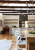 Moderner Stilmix in offener Wohnküche mit Designer-Barhockern an der Theke und weiße 50er Jahre Stuhlklassiker mit Tierfellbezug zu rustikalem Tisch