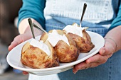 A person holding a plate of jacket potatoes with sour cream