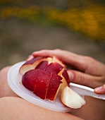 Person Slicing a Plum with a Plastic Knife on a Plastic Lid on her Lap