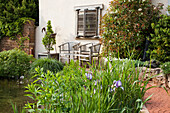 Wooden furniture next to a pond in the garden with flowering plants