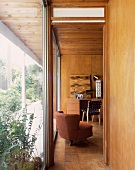 Blick durch offene Tür auf braunen Sessel im holzvertäfelten Wohnraum im 50er Jahre Stil