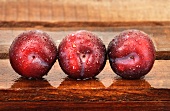 Three plums with droplets of water on wooden crate