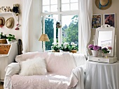 Sofa with pink throw below window next to mirror and flower arrangement on side table
