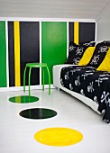 Sofa mit schwarzer Decke und Kissen und grüner Hocker in einem Dachzimmer mit bunt gestreifter Wand