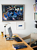 Workplace with computer, table lamp and abstract painting on the wall