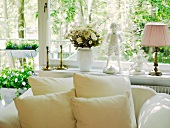 Cushions on white, upholstered armchair below large window decorated with flowers and vintage-style ornaments