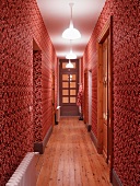 Narrow hall with ornate red and white patterned wallpaper and artificial lighting